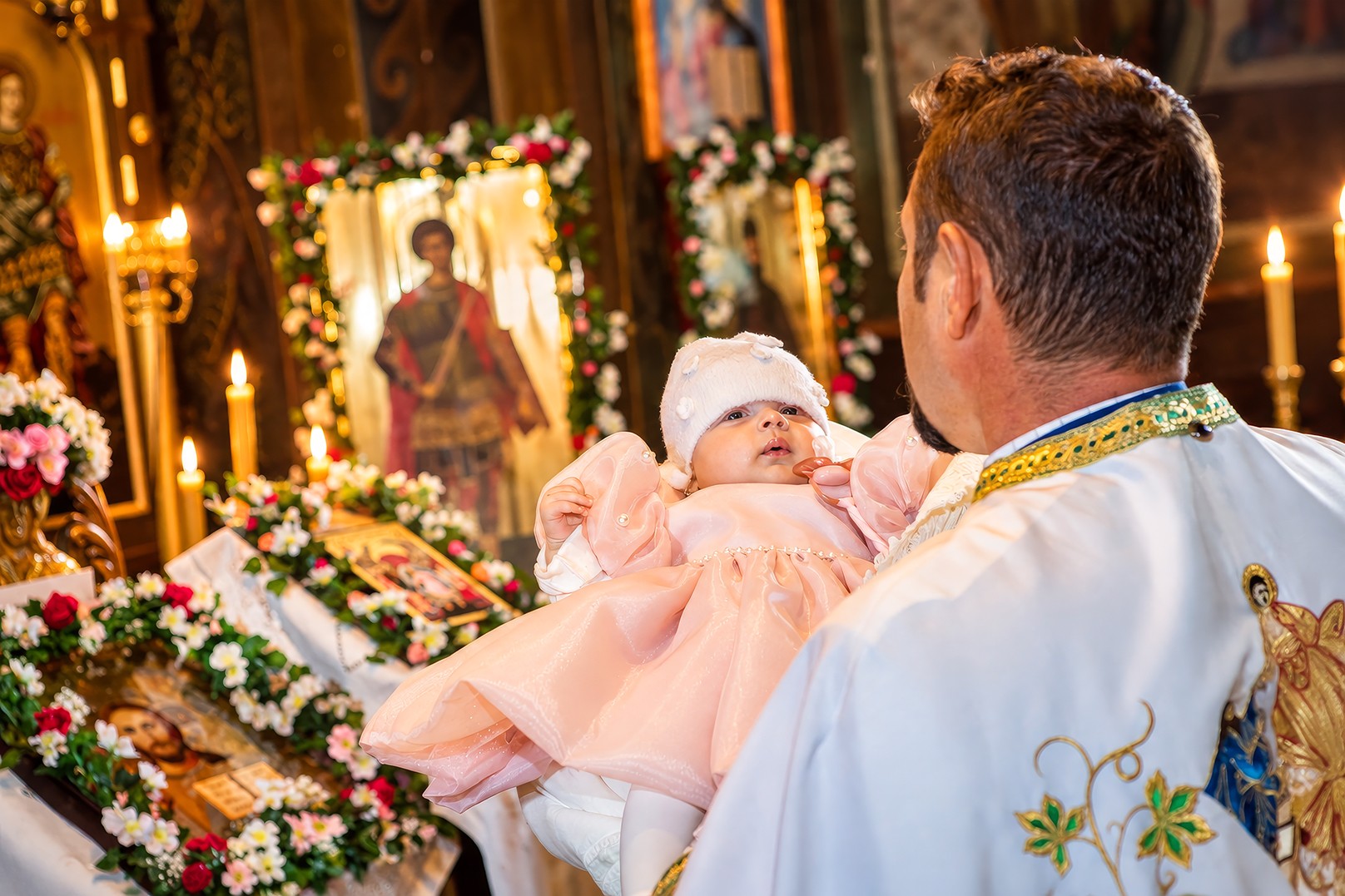 Preot ținând un bebeluș în brațe la botez într-o biserică ortodoxă